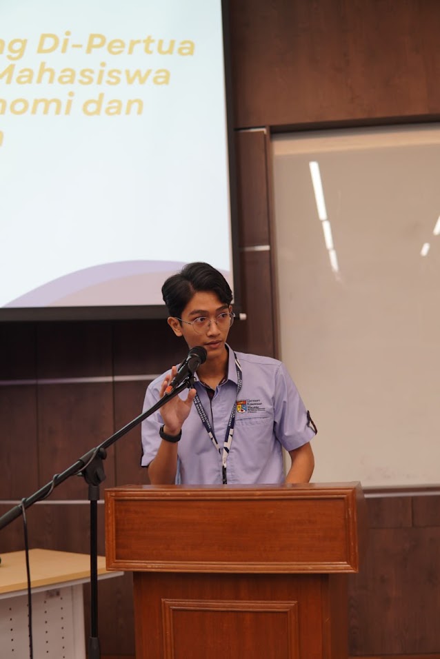 Aidil speaking at a lectern during a student association event.